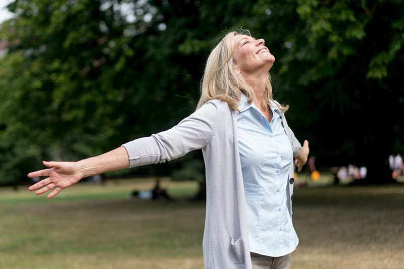 Woman outside, smiling with her arms open wide