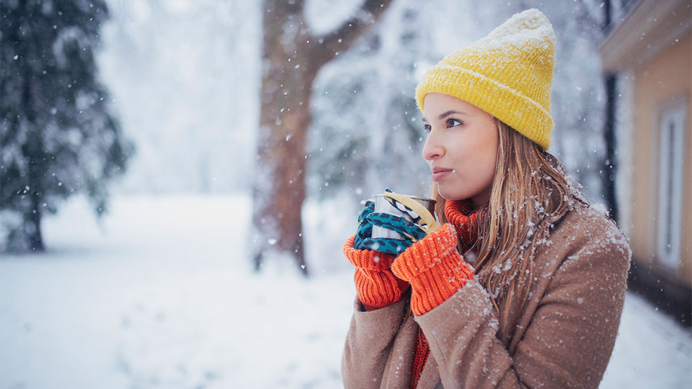 woman bundled in winter clothes warming up with hot drink