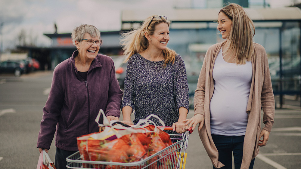 multigenerational women grocery shopping: an older woman, a middle-aged woman and a young pregnant woman