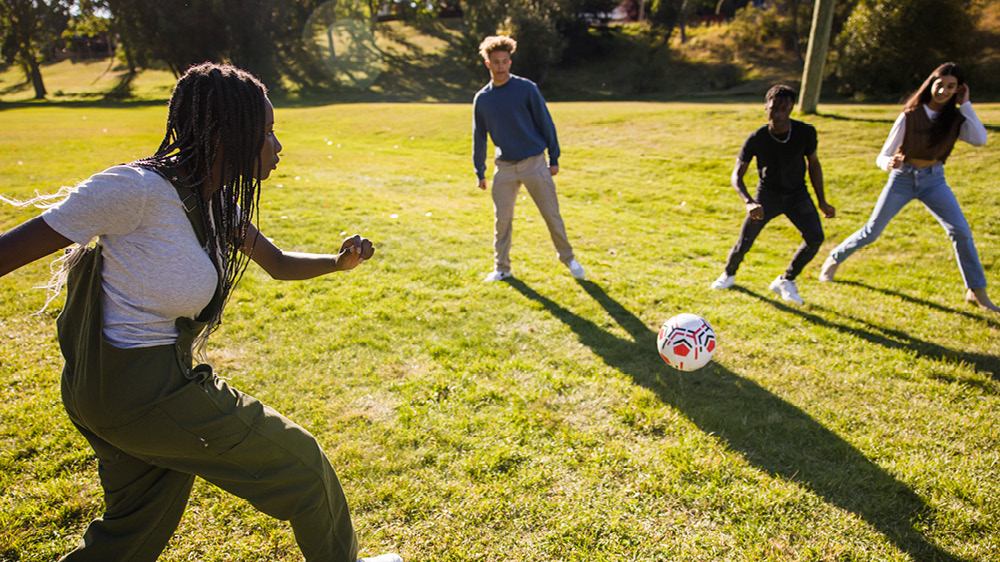 teenage friends playing soccer in sunny park