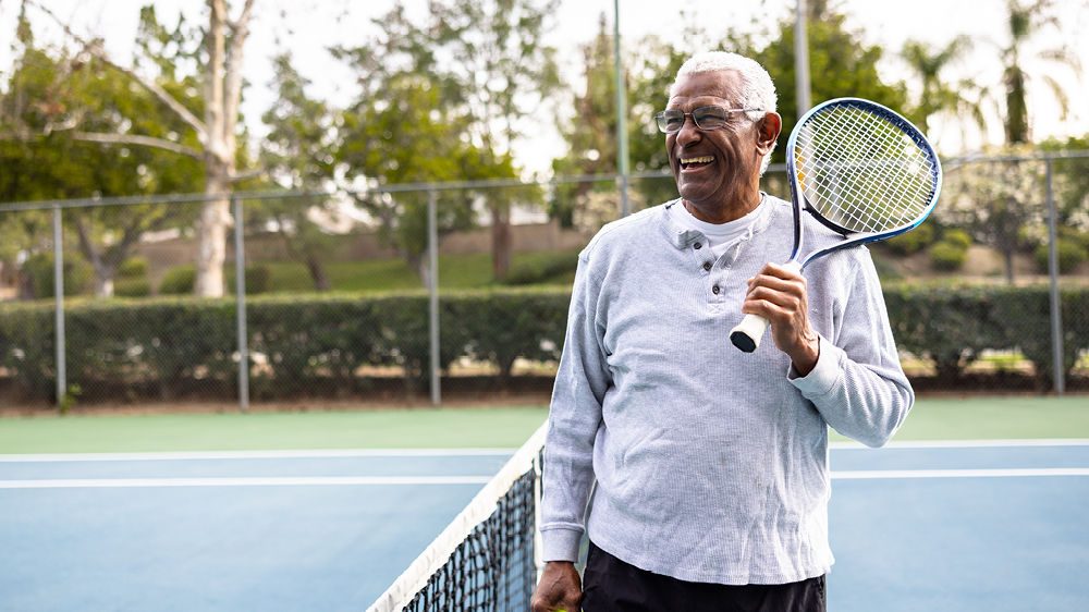 man on tennis court smiling with tennis racquet 