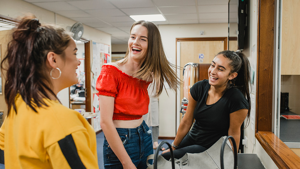 three young adult women talking in classroom 