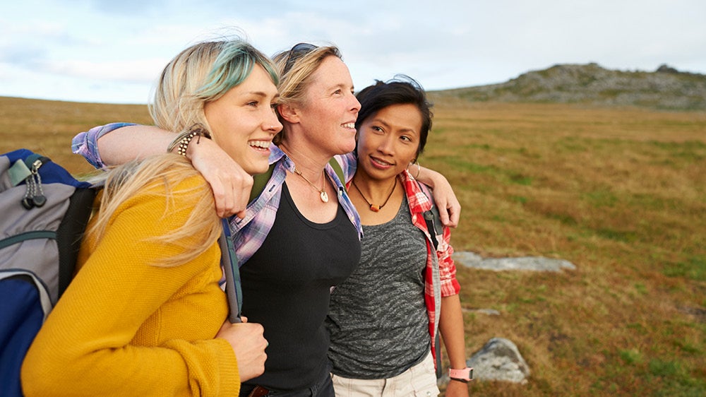 three diverse women embracing each other in a field and smiling