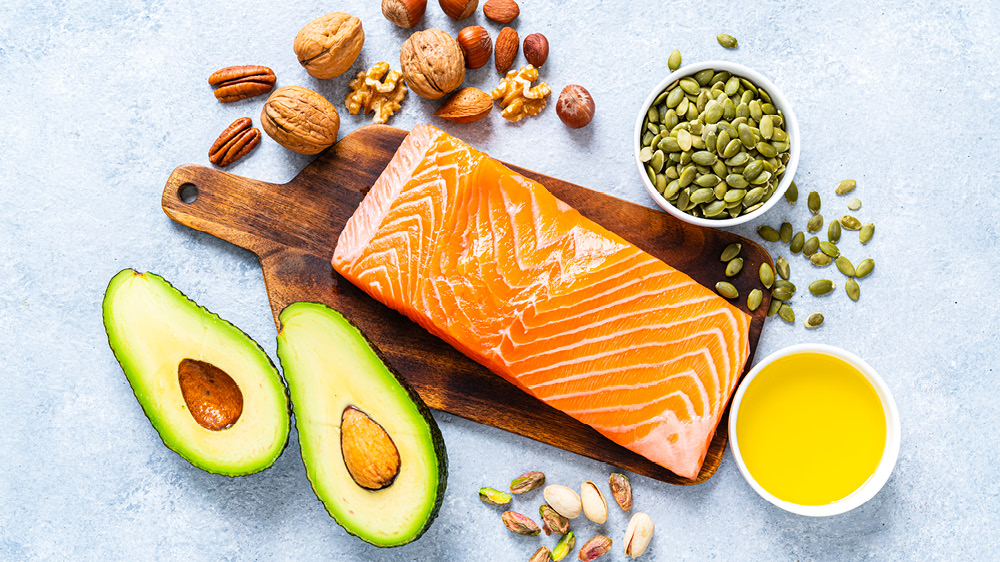 arrangement of food on cutting board and counter: avocado, salmon, nuts and olive oil