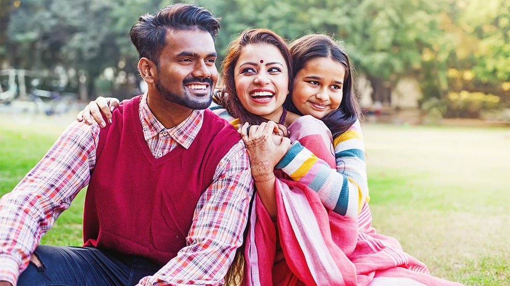 family of three, father, mother and young girl, sitting in grass