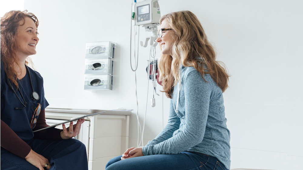 Smiling female nurse talking to teenage patient in clinic 